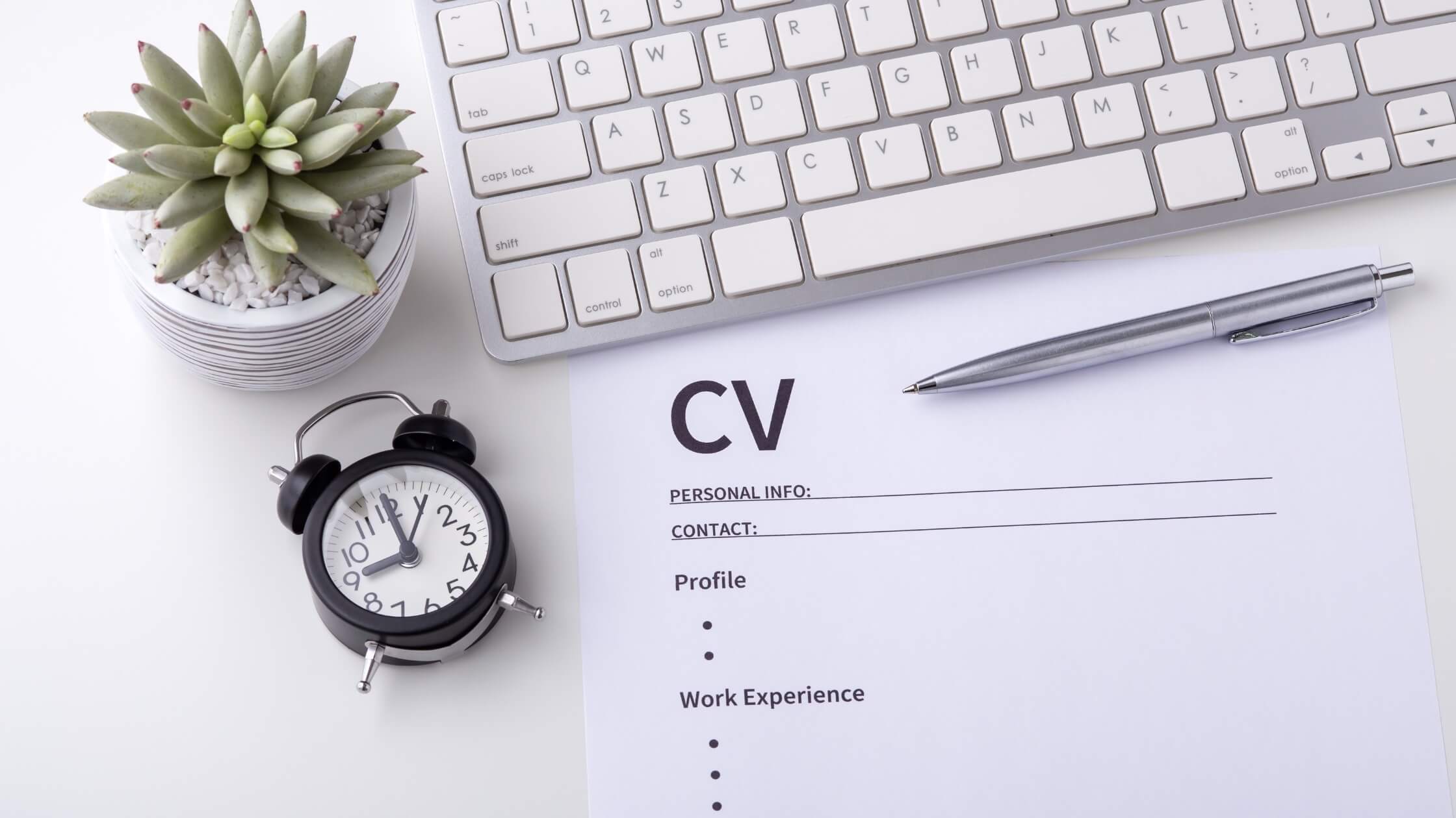 CV on a desk next to a pen, plant, clock and keyboard